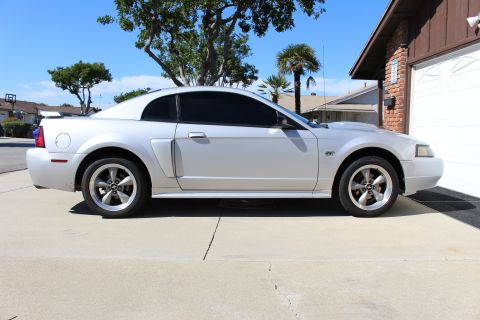 2002 Ford Mustang - Side view of a silver 2002 Ford Mustang with tinted windows parked in front of a garage.