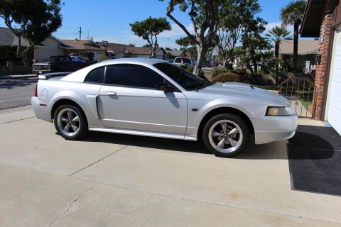 2002 Ford Mustang - A silver 2002 Ford Mustang coupe is parked in a driveway, its tinted windows and classic body style.