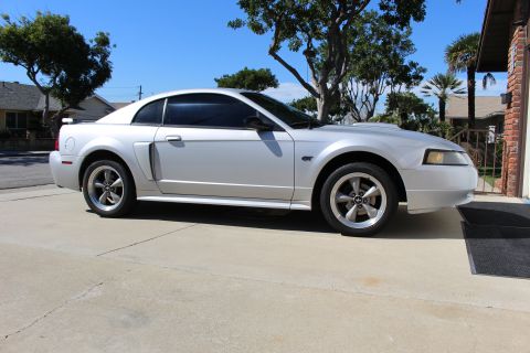 2002 Ford Mustang - A silver 2002 Ford Mustang is parked in front of a brick building on a sunny day.