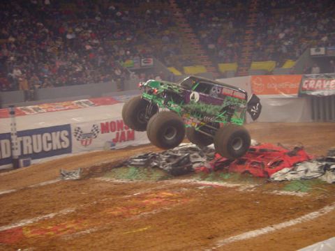 1989 Ford Bronco - A monster truck performs a jump over a mound of wrecked cars during a show.