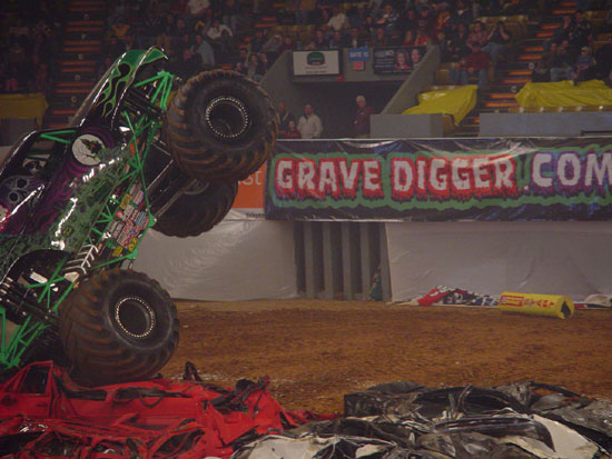 Monster truck on its side crushing cars, with a "Grave Digger" banner in the background