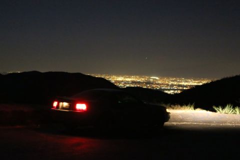 2002 Ford Mustang - A coupe's taillights glow against the backdrop of a city illuminated at night.