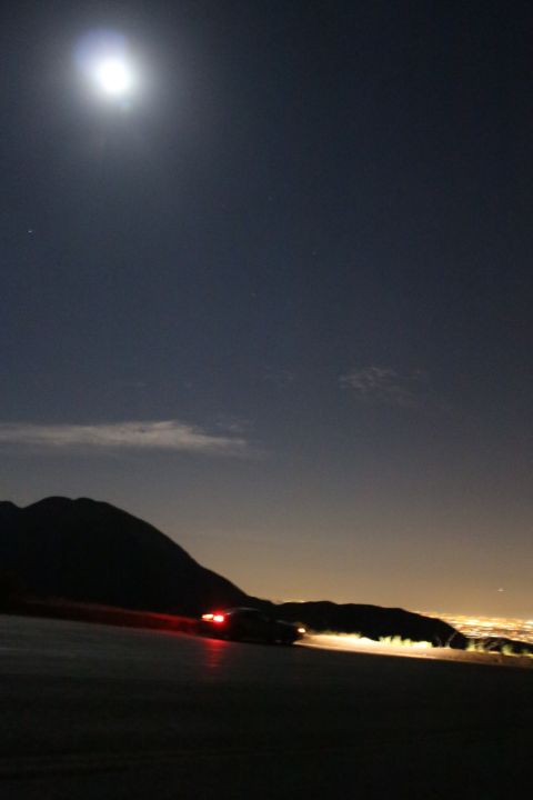 2002 Ford Mustang - A car navigates a winding mountain road at night, illuminated by its taillights and the bright moon above.