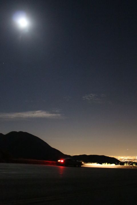 2002 Ford Mustang - A car drives on a mountain road at night, with the lights of a city spread out below.