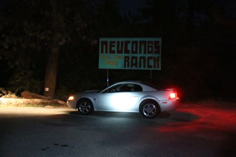 2002 Ford Mustang - A silver 2002 Ford Mustang is seen at night with its headlights on, parked near a sign for Neucombs Ranch.