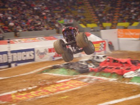 1989 Ford Bronco - A monster truck soars through the air above a pile of crushed cars during a show.