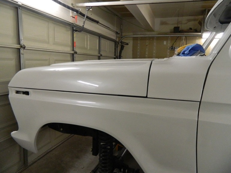 White 1979 Ford Bronco fender and hood in garage. Supermotors.net logo visible