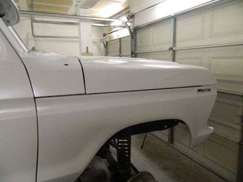 1979 Ford Bronco - Close-up of a white pickup truck's front fender and hood, revealing suspension details and a garage setting.