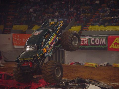 1989 Ford Bronco - Monster truck named Avenger performs a jump over wrecked vehicles in an arena.