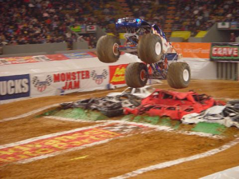 1989 Ford Bronco - A monster truck performs a jump over a heap of destroyed vehicles during an event.