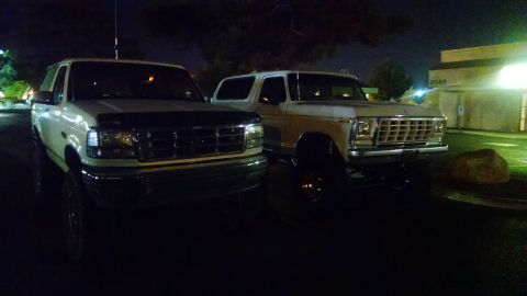 1979 Ford Bronco - Two white Ford SUVs are parked outside a building at night. The vehicle on the right is a 1979 Ford Bronco.