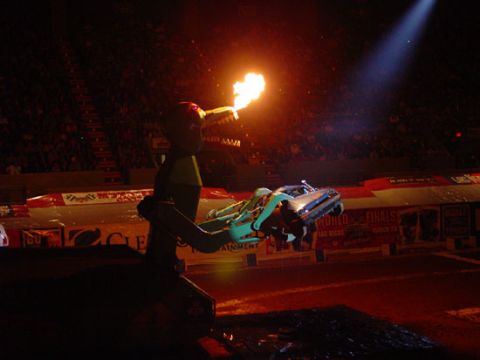 1989 Ford Bronco - A car is lifted by a mechanical arm that shoots fire during a monster truck show.