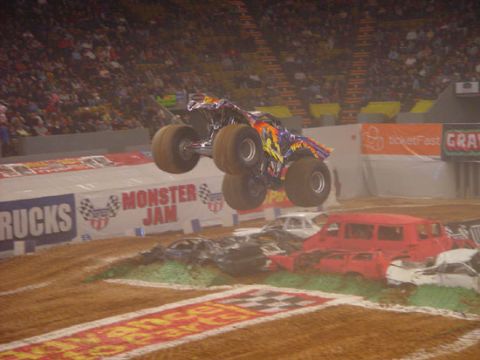 1989 Ford Bronco - A monster truck soars through the air above a pile of crushed cars during a Monster Jam event.