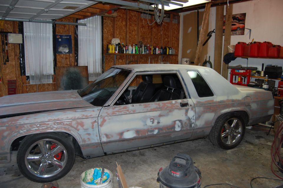 Car body in primer, sitting in a garage with tools and shelves in the background