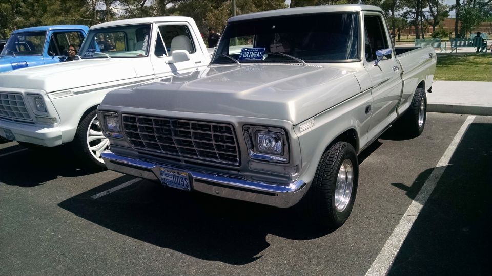 Silver 1979 Ford Bronco parked next to a white truck and a blue truck