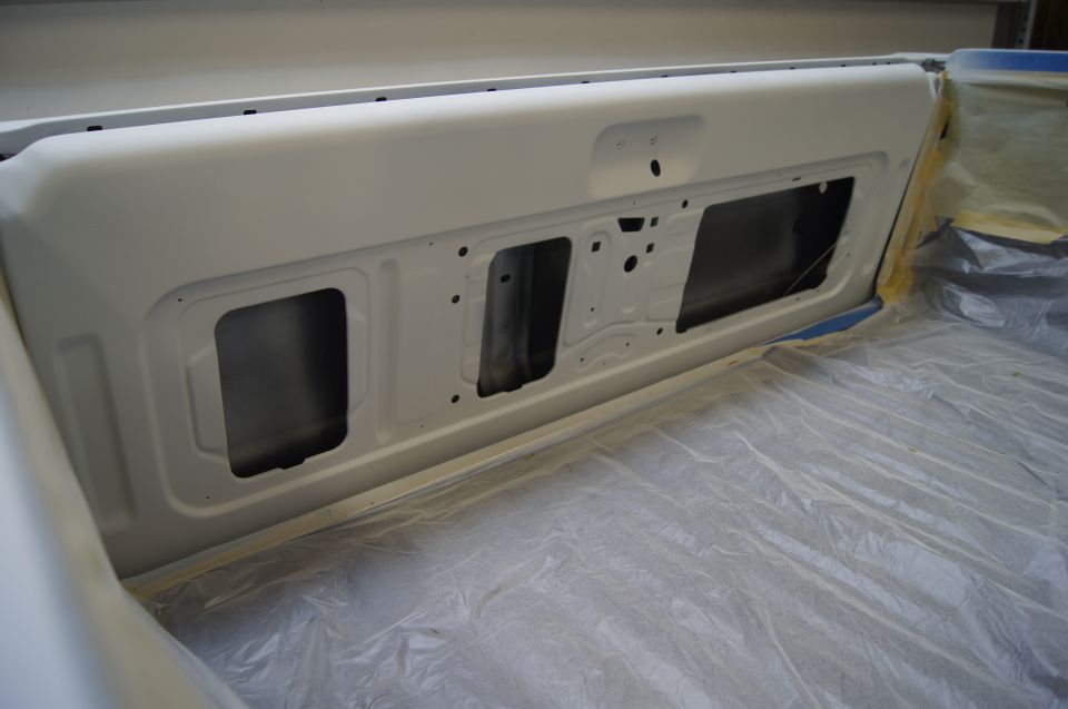 Interior of a white tailgate, showing stamped metal and cutouts for lights or trim