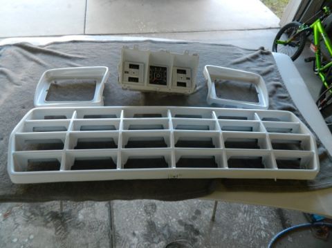1979 Ford Bronco - White grille, headlight bezels, and instrument cluster are displayed on a cloth surface, possibly for restoration or sale.