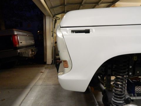 1979 Ford Bronco - A white truck's front fender and suspension are visible, with another vehicle parked behind it in a garage.