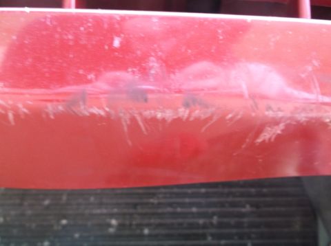 1999 Mercury Grand Marquis - Close-up of a damaged red car bumper with visible scratches and scuffs.