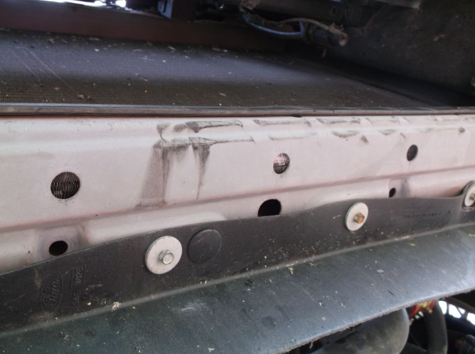 Close-up of car's radiator support area with some dirt and rust marks