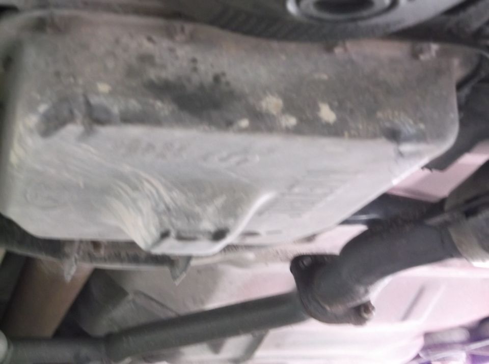 Underside view of a vehicle's oil pan and exhaust pipe. Supermotors.net logo visible