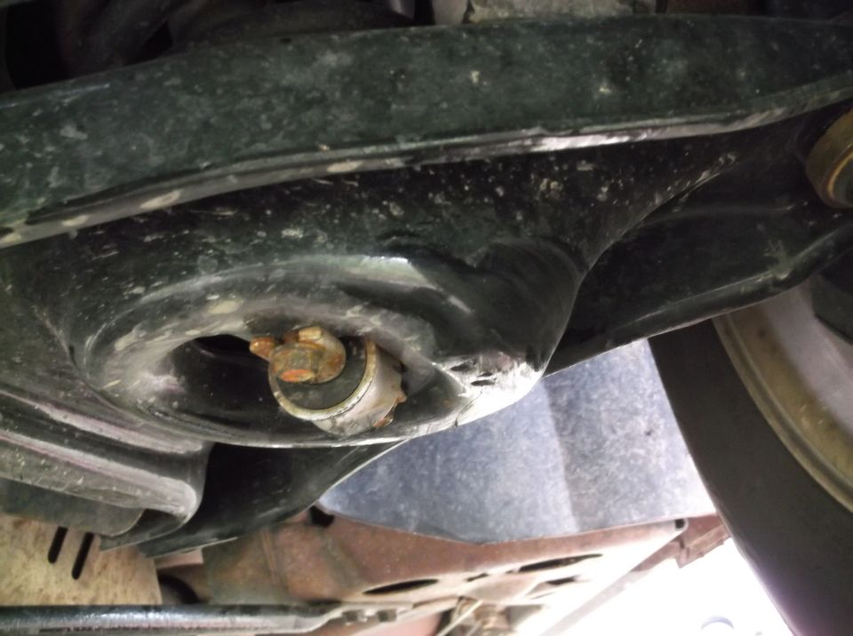Close-up of a rusty bolt in a car's suspension system, with a tire visible