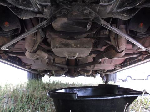 1999 Mercury Grand Marquis - An oil drain pan sits beneath the exhaust system and transmission of a car, ready to catch used oil.