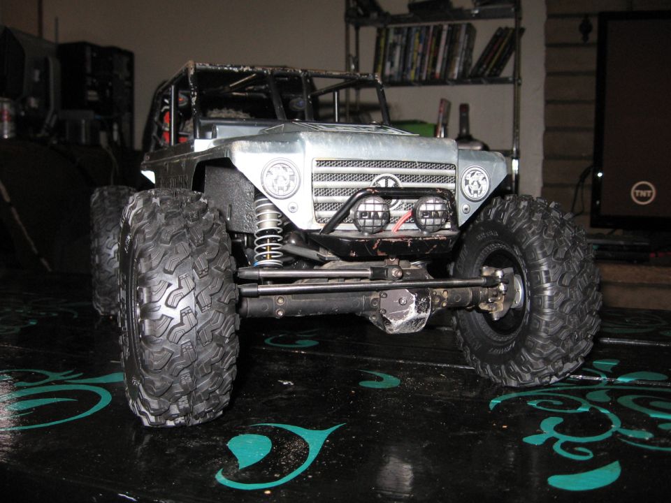 Silver toy RC rock crawler with large tires and a roll cage, viewed from the front