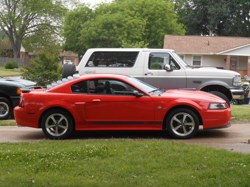 Red 2000 Ford Mustang coupe parked next to a white Ford Bronco