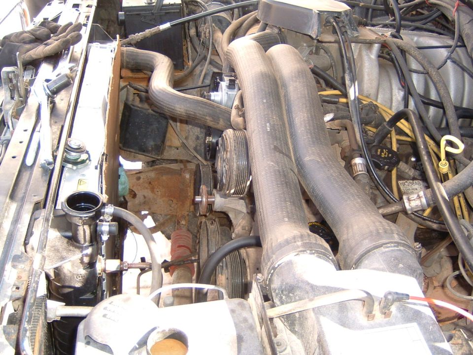 Engine bay with hoses, belts, and radiator visible. Some rust is present