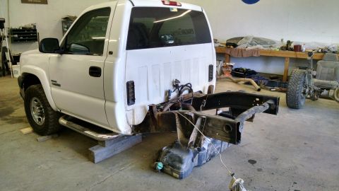 1985 Jeep CJ7 - White pickup truck chassis with fuel tank removed, undergoing repairs in a workshop.