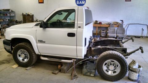 1985 Jeep CJ7 - White pickup truck chassis with "Duramax" badging, viewed from the side in a workshop.