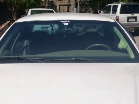 2000 Mercury Grand Marquis - Front view of a white 2000 Mercury Grand Marquis, showing the interior and windshield. Other vehicles are parked behind it.