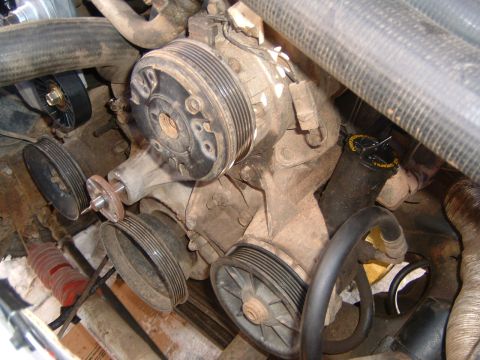 1987 Ford Bronco - Close-up view of an engine's water pump assembly, showing various pulleys and hoses. A reservoir cap with readable text is also visible.
