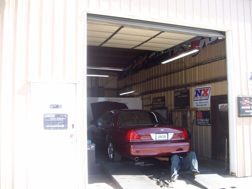 Maroon Ford Crown Victoria with a "JUNIOR" license plate, viewed from the rear in a garage