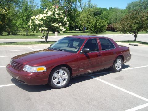 2004 Ford Crown Victoria - Dark red Ford Crown Victoria sedan parked at an angle in an empty paved lot, shown from the driver's-side front three-quarter view with a b…