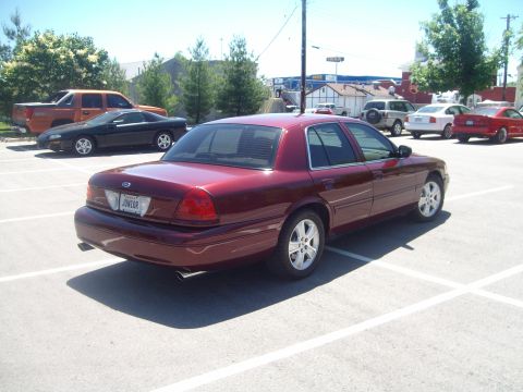 2004 Ford Crown Victoria - Dark red Ford Crown Victoria sedan seen from the passenger-side rear three-quarter angle in a parking lot, showing dual chrome-tipped exhau…