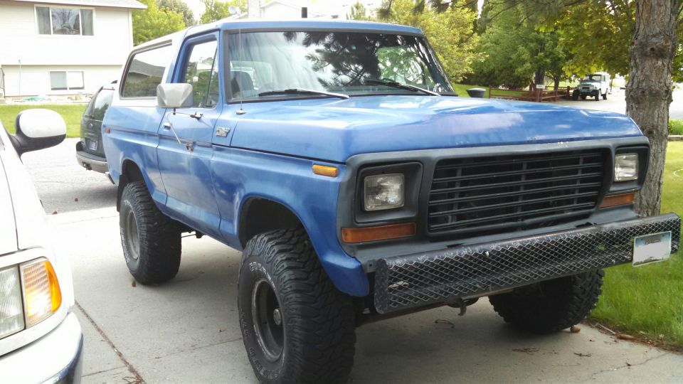 Blue lifted Ford Bronco with black grille, expanded-metal bumper and large all-terrain tires in a driveway