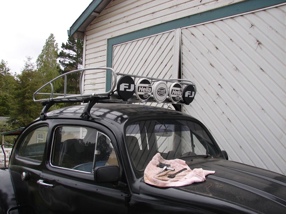 Black 1964 Volkswagen Beetle with roof rack and four lights, seen from a 3/4 front angle