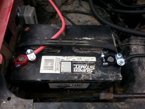 1981 Ford Bronco - Close-up view of a car battery and its terminals with connected jumper cables.