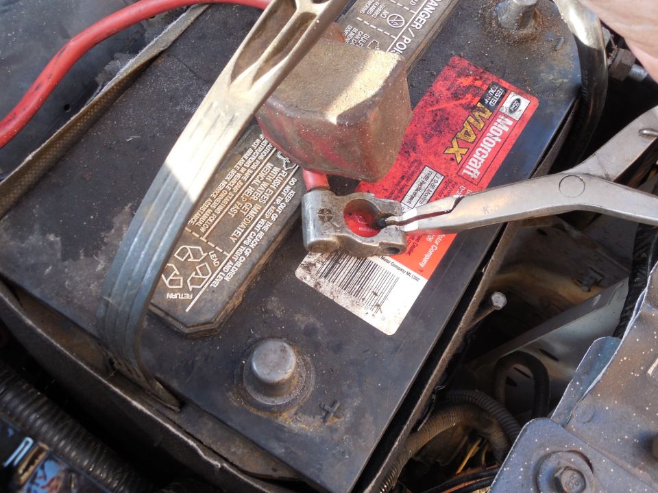 Pliers loosening a battery terminal clamp on a Motorcraft battery