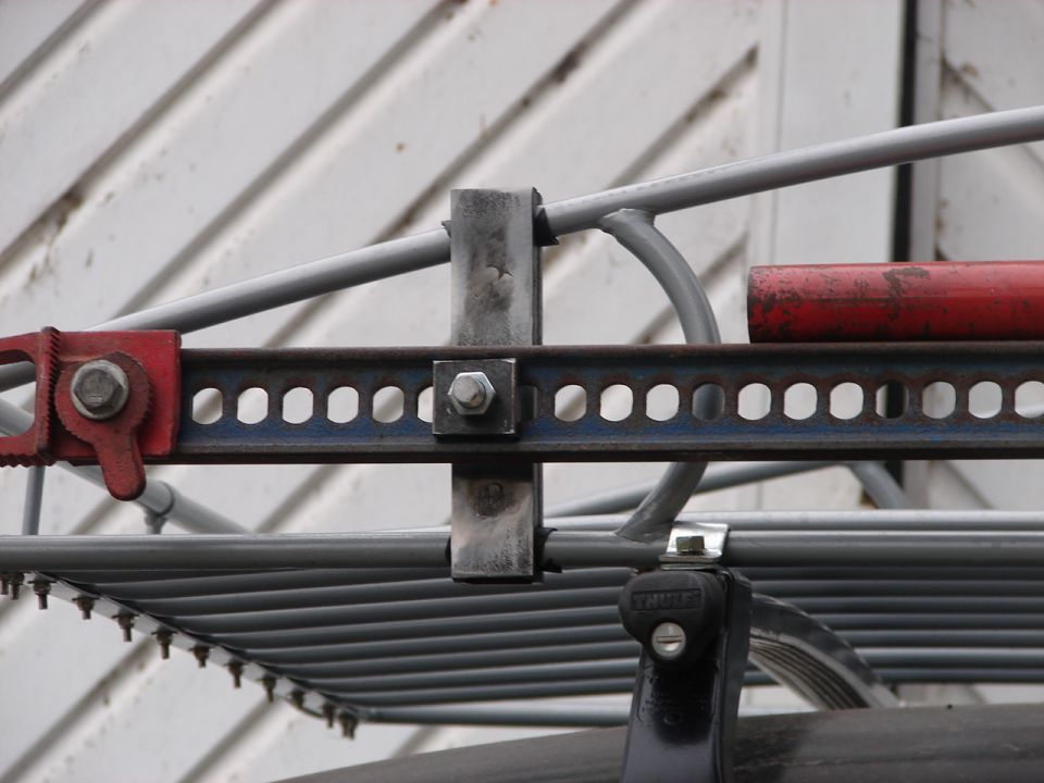 Close-up of a hi-lift jack attached to a metal roof rack system