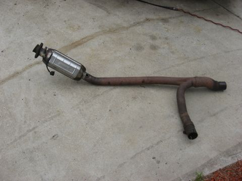1994 Ford Bronco - Exhaust pipe assembly, including a catalytic converter, lying on a concrete surface.