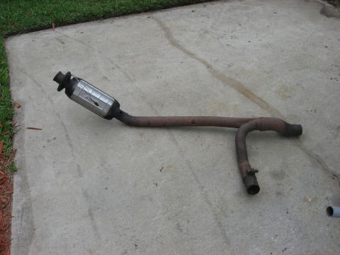 1994 Ford Bronco - Removed exhaust system part, likely a catalytic converter and pipe assembly, on a paved surface.