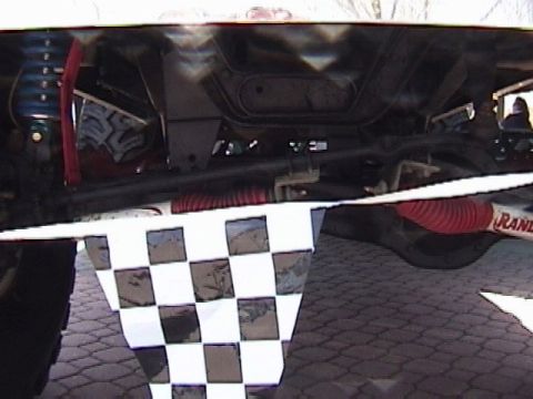 1995 Ford Bronco - A close-up of a vehicle's undercarriage, suspension parts and a checkered flag draped over the front.