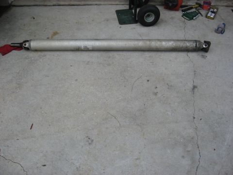 1994 Ford Bronco - A driveshaft is shown removed from a vehicle, lying on a garage floor. Tools and a dolly are visible in the background.
