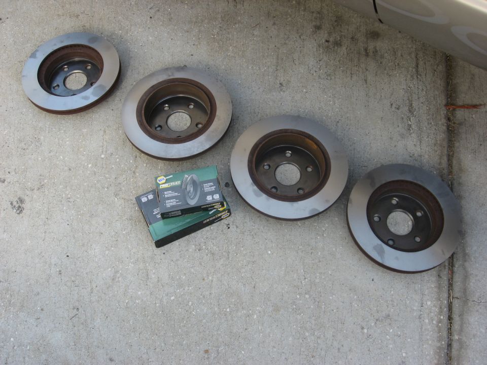 Four brake rotors and two boxes of brake pads on a concrete surface