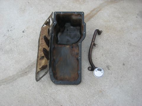 1994 Ford Bronco - An oil pan and its associated pickup tube are displayed on a concrete surface, indicating they are automotive parts.