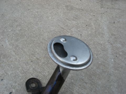 1994 Ford Bronco - Close-up of an oil pump pickup tube with a metal screen, resting on a concrete surface.
