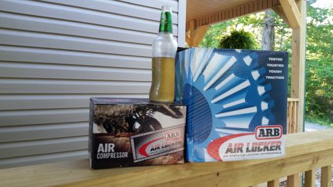2003 Nissan Frontier - Boxes for ARB air locker and air compressor are displayed on a porch railing with a bottle of liquid.